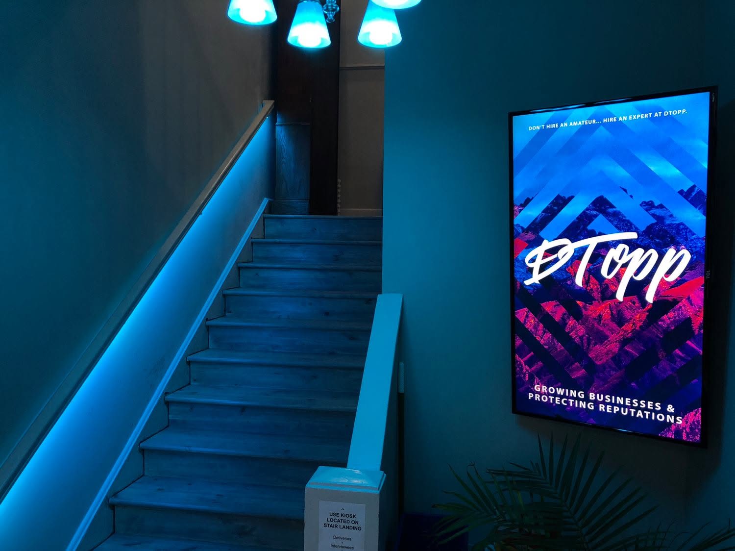 Staircase lit in blue beside a wall screen showing the DTopp logo